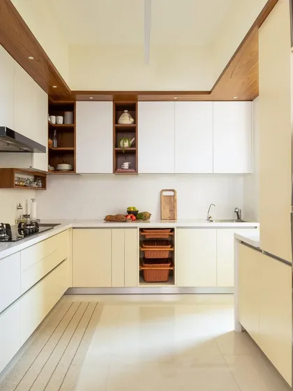 A minimalist kitchen featuring cream-colored cabinets, open wooden shelving, and integrated wicker baskets. The design prioritizes clean lines and a clutter-free aesthetic.