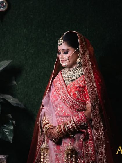 A moody and elegant portrait of the bride, with her name and her groom's name in text. The dark background makes her red lehenga pop.