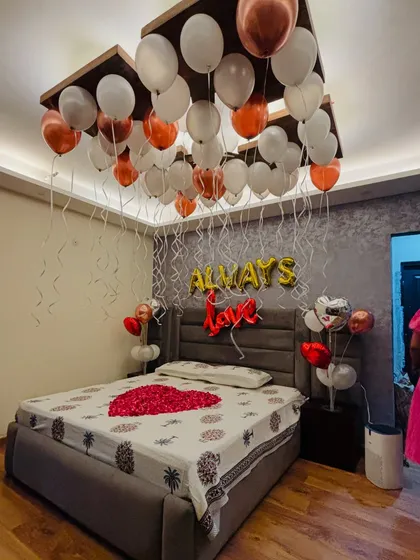 A full view of a romantic anniversary room setup, showing the decorated bed, 'Always Love' balloons, and ceiling balloons.