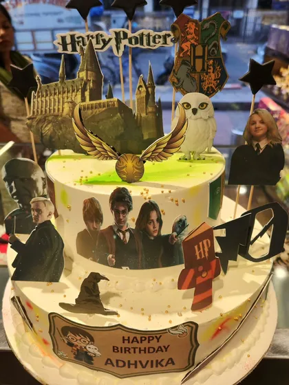 A magical two-tier Harry Potter theme cake for the ultimate fan. This creation is packed with iconic, edible imagery from the wizarding world, including Hogwarts castle, the golden snitch, and beloved characters.