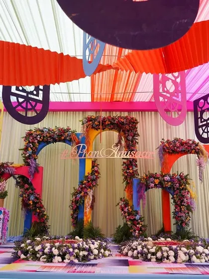 The main stage for the Haldi ceremony, featuring a backdrop of colorful, abstract arches adorned with flowers. The multi-colored flooring and ceiling drapes complete this vibrant, carnival-themed setup.