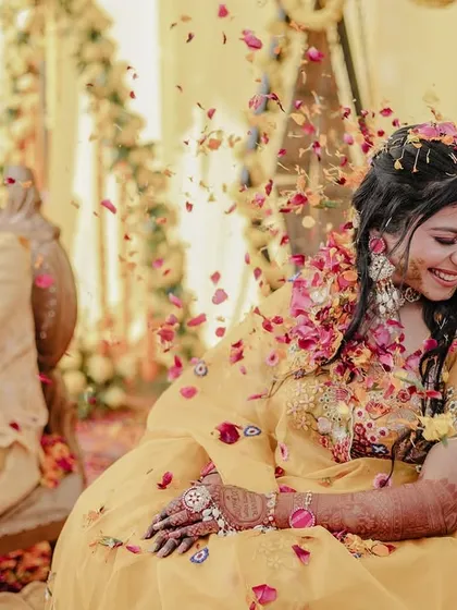 A candid shot of the bride smiling as flower petals are thrown, with the groom in the background.