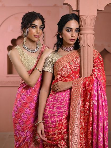 Two models together, one in a pink bandhani and the other in a red and pink brocade saree, showcasing the variety in my festive collection.