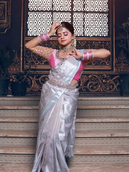 A graceful dance pose in a silver tissue saree, paired with a pink blouse and sparkling diamond and emerald jewellery.