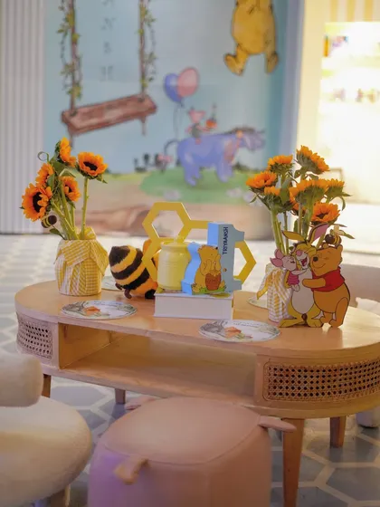 A cozy corner with a Winnie the Pooh and Piglet cutout, sunflowers, and a honeycomb-themed '1' sign.
