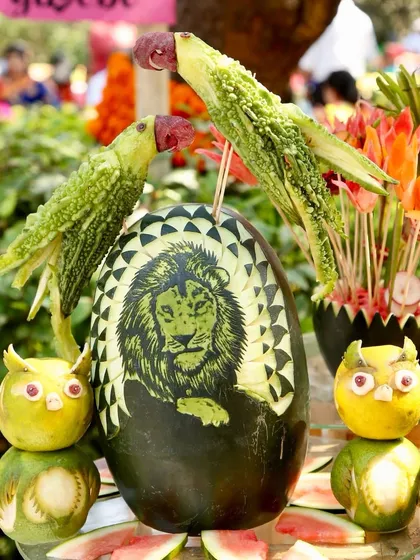 A stunning display of fruit and vegetable art, featuring a lion carved into a watermelon, parrots made from bitter gourds, and owls from apples. This adds a 'wow' factor to the decor.