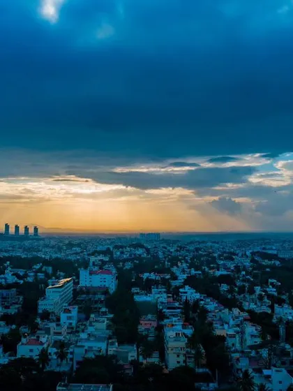 A stunning aerial panorama of the Bangalore cityscape at sunset, with golden sun rays breaking through dramatic blue clouds. This shot showcases my capability in urban and cityscape cinematography.