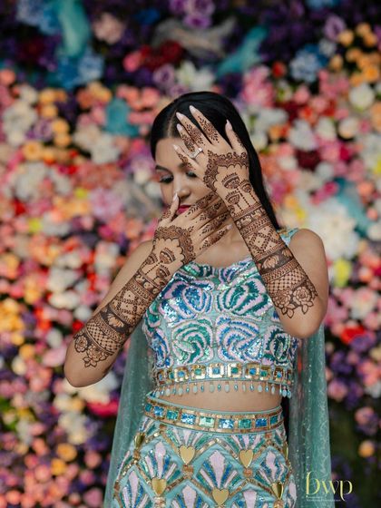 A creative pose against a floral wall, highlighting the bride's themed mehndi.