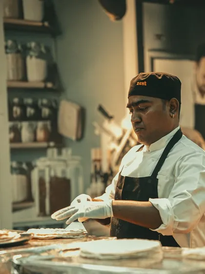 A chef wearing a "Zest" branded cap, carefully preparing food.