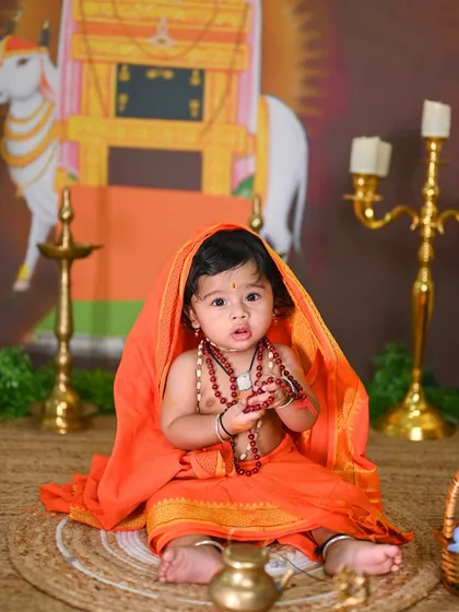A toddler dressed as Raghavendra Swamy, looking curiously at the camera.