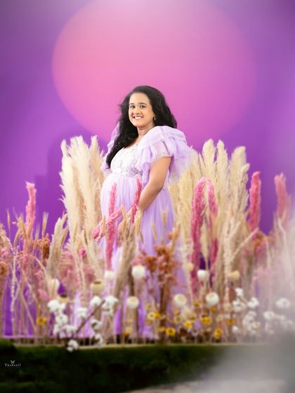 A beautiful portrait of a mom-to-be standing in a whimsical field of pampas grass and flowers against a purple backdrop, radiating happiness and anticipation.