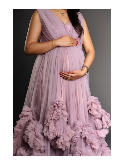 A close-up shot of a mother-to-be's torso, highlighting the beautiful texture of the ruffled lavender gown against her baby bump.