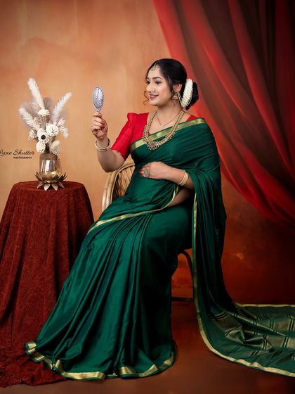 A portrait inspired by the classic paintings of Raja Ravi Varma. The mother-to-be, in a beautiful green saree, gazes into a handheld mirror, creating a scene of timeless elegance.