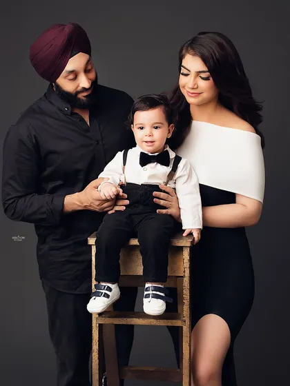 A classic family portrait with a stylish twist. The family's coordinated outfits and the little boy's confident pose on the stool make for a sharp and memorable photo.