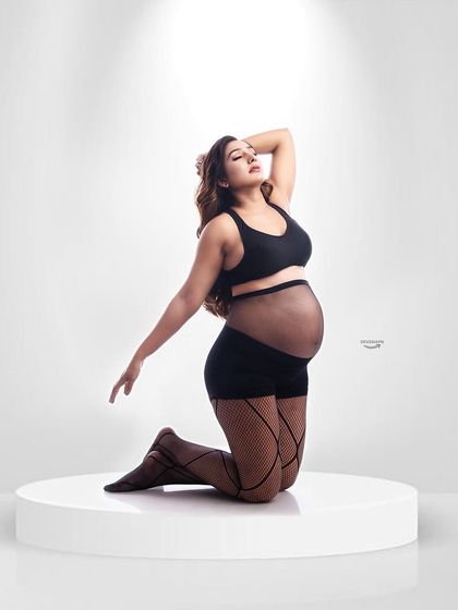 A bold and modern maternity portrait. The client is wearing stylish lingerie and fishnet stockings, creating a powerful and confident image that celebrates her changing body.