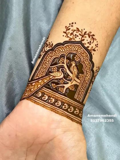 A delicate wrist cuff design featuring two birds, a peacock and a peahen, perched on a branch inside a traditional window frame.