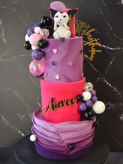 A whimsical three-tier Kuromi-themed cake for Anvee's birthday. The cake features shades of purple and pink, a fondant ruffle effect, and a cute Kuromi topper.