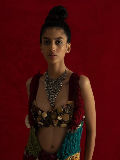 This shot is a burst of color and texture. The bold red background makes the model and her eclectic, handcrafted outfit stand out. The direct, centered pose is strong and confident, perfect for a designer lookbook.