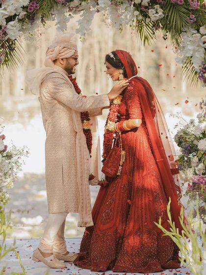 A beautiful, full-length shot of the couple during their Jaimala exchange, showcasing their outfits and the gorgeous floral decor.
