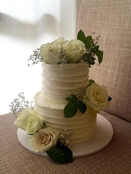 A classic and romantic two-tiered engagement cake. This 1.5kg chocolate cake has a rustic textured buttercream finish and is adorned with fresh white roses and baby's breath.
