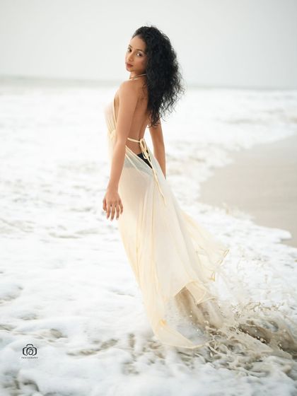 A beautiful shot of a model in a flowing white dress walking through the surf. The movement of the dress and the water creates a dynamic and ethereal image.