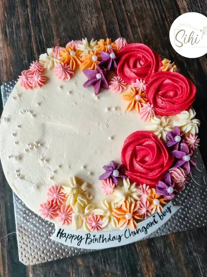 Pretty patterns in buttercream. This cake features a crescent of beautifully piped rosettes and flowers in a warm, vibrant color palette.