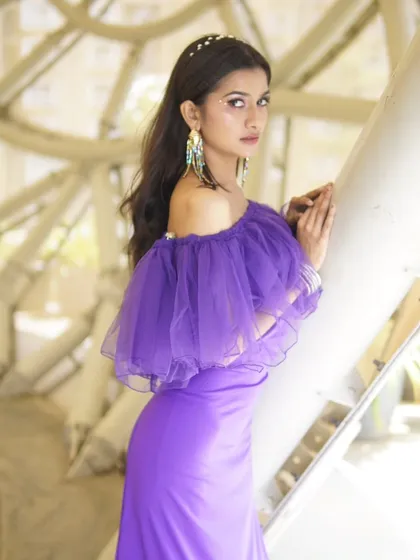 This shot from a lookbook session showcases a modern, chic makeup style. The focus is on a clean, sculpted face with a subtle graphic liner, paired with statement earrings to complement this purple designer gown.