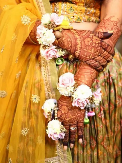 A beautiful shot of a bride's hands, adorned with floral jewelry. The details of the mehendi, the flowers, and the outfit all come together to create a stunning image.