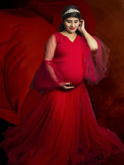 A powerful solo maternity portrait with a vibrant red gown and dramatic fabric flow against a rich, dark background.