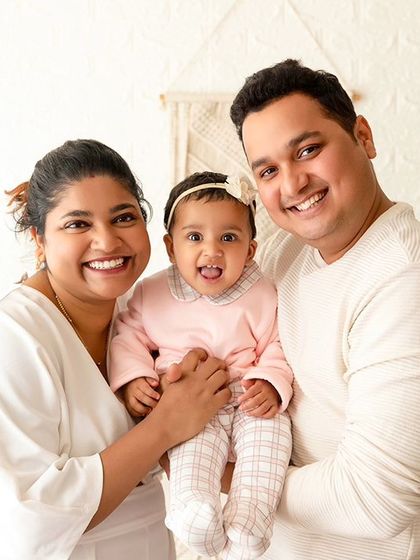 A bright and happy family portrait against a white brick wall. The simple, light-filled setting keeps the focus on the family's joyful expressions.