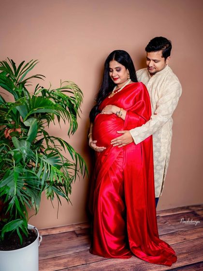 A loving couple's portrait in a studio setting. Her vibrant red satin saree and his simple kurta create a beautiful, classic look.