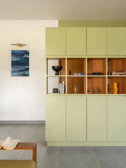 The custom-designed foyer unit serves as both storage and a visual divider. Its sage green finish adds a soft block of color, while the open wooden shelves are used for displaying decor.