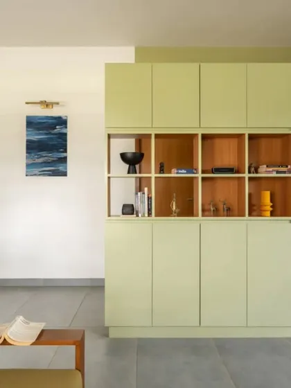 A custom-designed storage cabinet in a soft green hue acts as a focal point and a functional divider in the open-plan living area. The open shelving provides space for decor, personalizing the home.