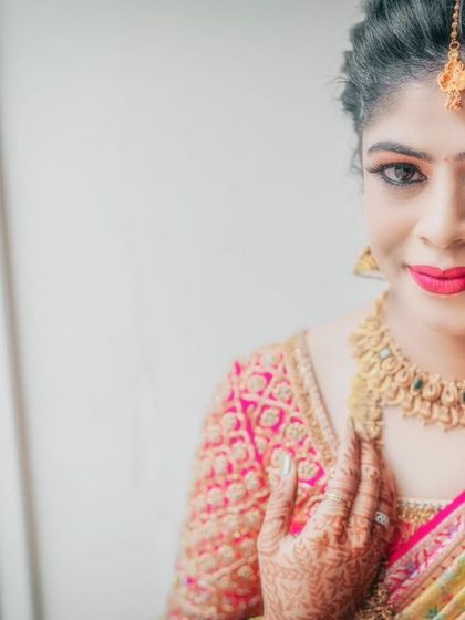 A close-up portrait of a bride, showcasing her stunning makeup and traditional gold jewelry.