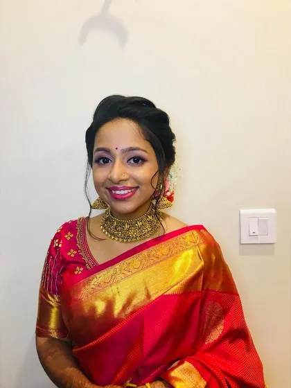 This bride is absolutely slaying her reception look in a vibrant red and gold silk saree. The makeup is elegant and classic, with a smile that shows how happy she is.