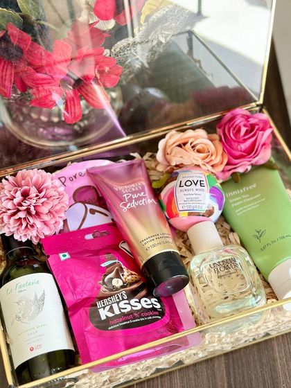 A luxury Rakhi hamper for your sister, presented in a beautiful glass box. It includes a bath bomb, Zara perfume, a mini wine bottle, a face sheet mask, and Victoria's Secret body cream.