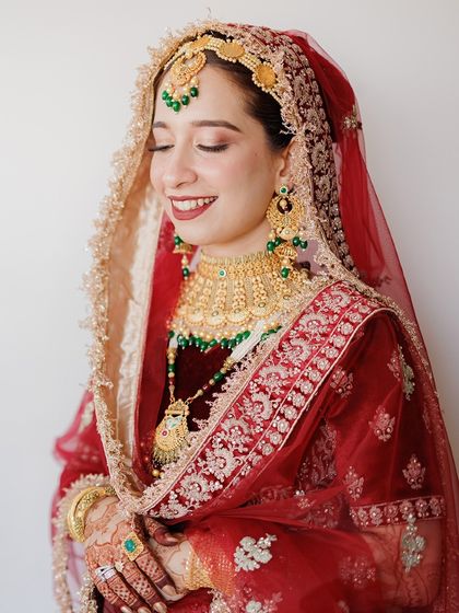 A radiant portrait of a Muslim bride, her eyes closed in a moment of bliss, showcasing her stunning red and gold wedding attire.