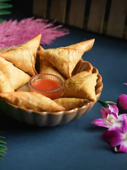 The classic triangular shape of my Chicken Irani Samosas, served with a sweet chili sauce. They are a timeless snack that I make fresh for every order.