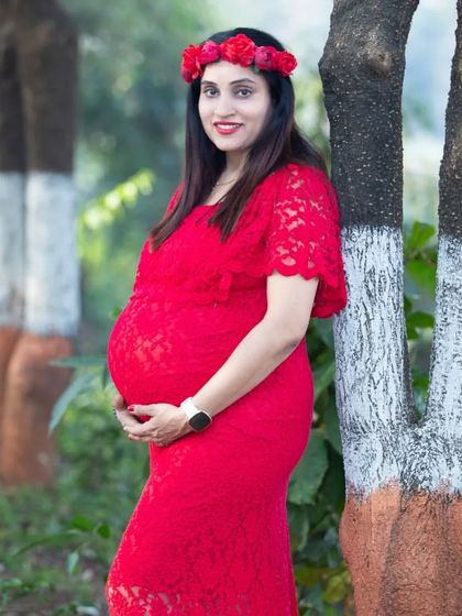 A beautiful mom-to-be in a red lace gown. The floral crown adds a bohemian touch, perfectly complementing the natural, wooded setting.