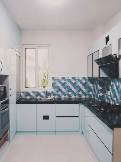 This U-shaped kitchen makes a statement with its vibrant, fish-scale patterned backsplash in shades of blue and green. We paired it with light blue cabinetry and a black granite countertop to create a space that is both playful and highly functional, proving that practical kitchens can also be full of personality.