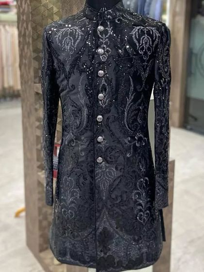 A black sherwani with intricate, shimmering black-on-black paisley embroidery. The detailed craftsmanship gives this classic piece a luxurious and textured look.