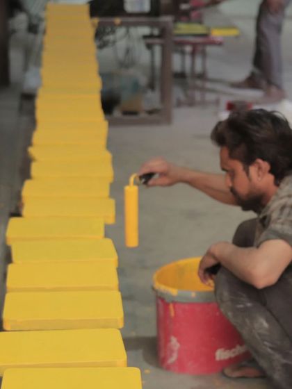An artisan carefully painting individual wooden blocks in a bright yellow, part of a larger modular wall art installation.