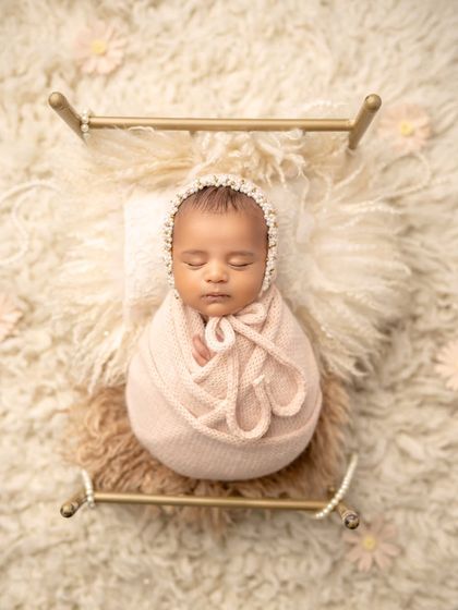A precious gift, perfectly wrapped. This newborn, snug in a pink swaddle and a delicate bonnet, looks like a little doll on a tiny bed.