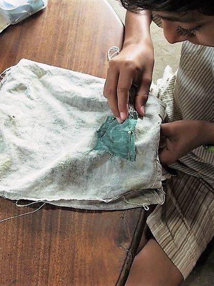 A young participant learns the art of patching, a fundamental skill in clothes mending. This simple technique can fix holes, cover stains, and add a unique decorative touch to any garment.