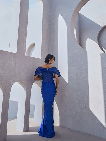 A sculpted mesh gown in active blue, featuring a striking shoulder structure, corseted precision, and front-gathered elegance. It is a bold symphony of form and movement.