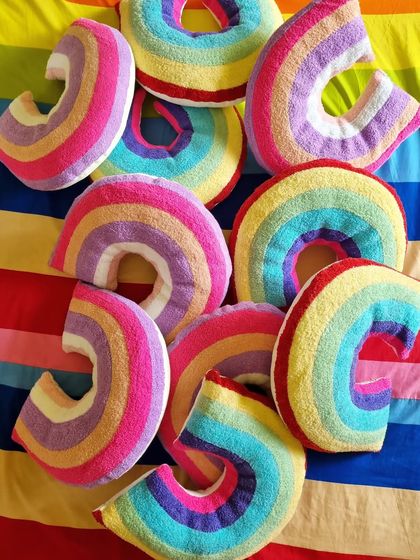 Rainbow heaven. A pile of our cozy and colorful rainbow-shaped cushions, perfect for adding a pop of color and fun to a kid's bed or playroom.