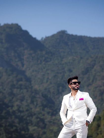 A confident and stylish portrait of the groom against the majestic mountains of Rishikesh. Dressed in a sharp white suit, he exudes modern elegance, showcasing a look that perfectly complements the grand landscape.