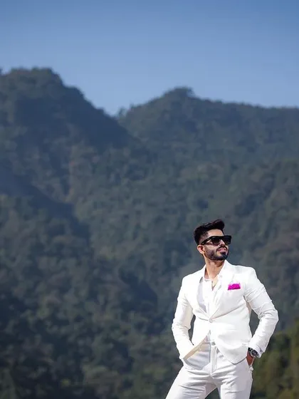 A confident and stylish portrait of the groom against the majestic mountains of Rishikesh. Dressed in a sharp white suit, he exudes modern elegance, showcasing a look that perfectly complements the grand landscape.