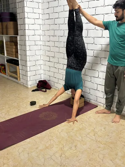 Inversions are made accessible and safe for everyone. I am spotting a student as she uses the wall and a yoga block for support in a handstand, building the strength and confidence needed to master the pose.