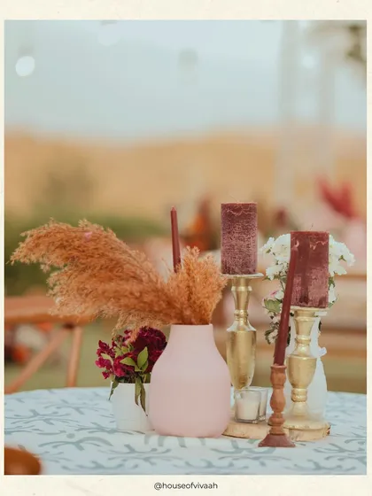 A close-up of a tablescape featuring pampas grass, burgundy candles, and brass holders, showcasing the earthy and warm details of the bohemian Mehendi theme.